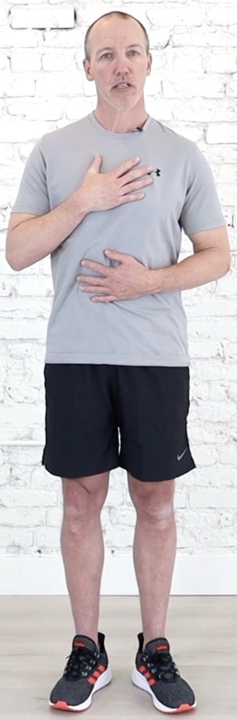 Person standing with one hand on the chest and one on the belly, lifting the rib cage slightly
